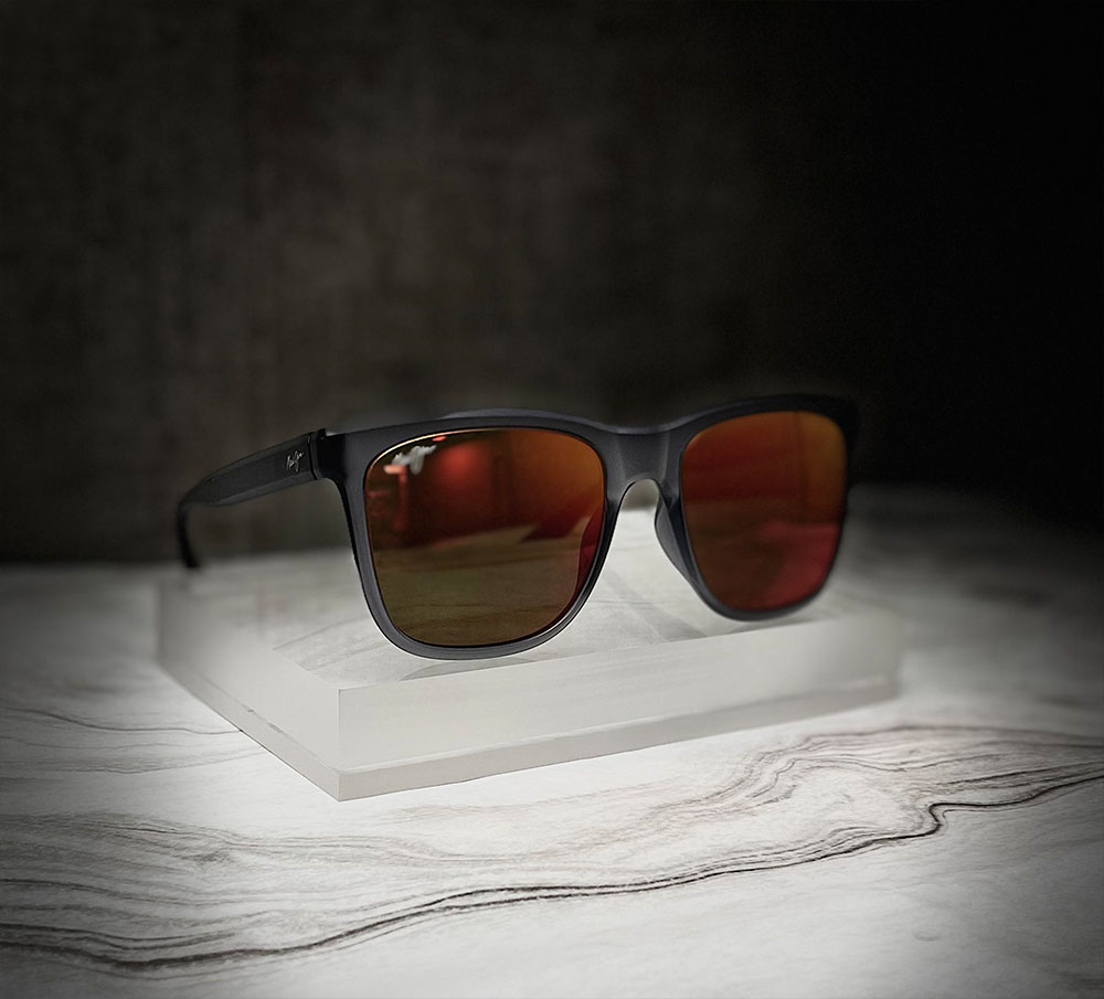 A pair of black sunglasses with a reflective surface, placed on a display stand against a marble background.