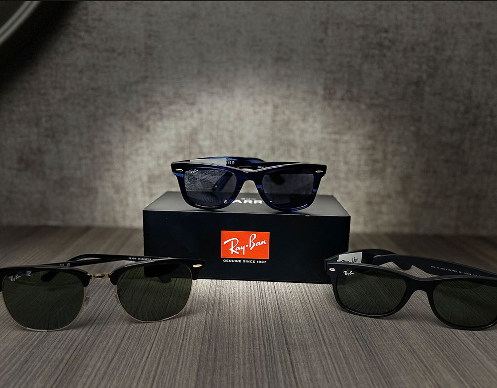 A photograph of a collection of sunglasses displayed in a box with three pairs visible, showcasing a variety of styles and colors against a neutral background.