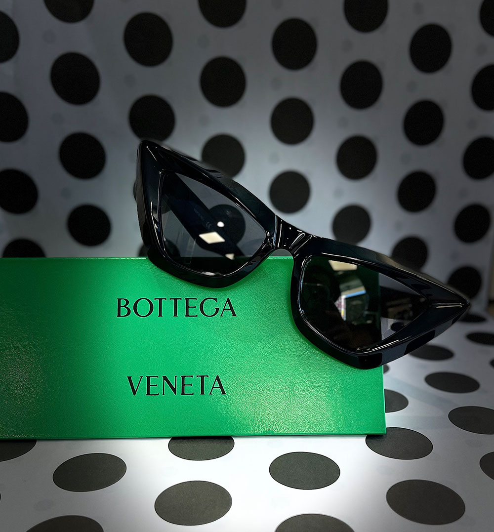 A pair of sunglasses with a green frame and black lenses, resting on a cardboard box with the text 'BOTTEGA VENETA' in white letters.