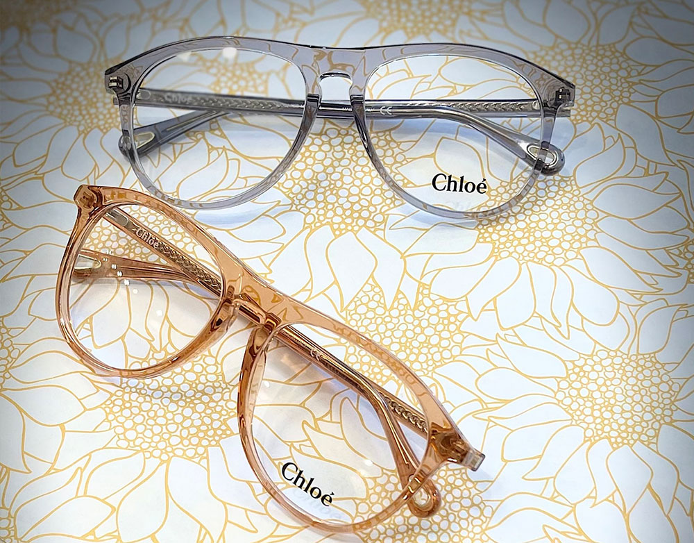 Two pairs of glasses, one with a clear frame and the other with a rose gold frame, resting on a patterned surface.