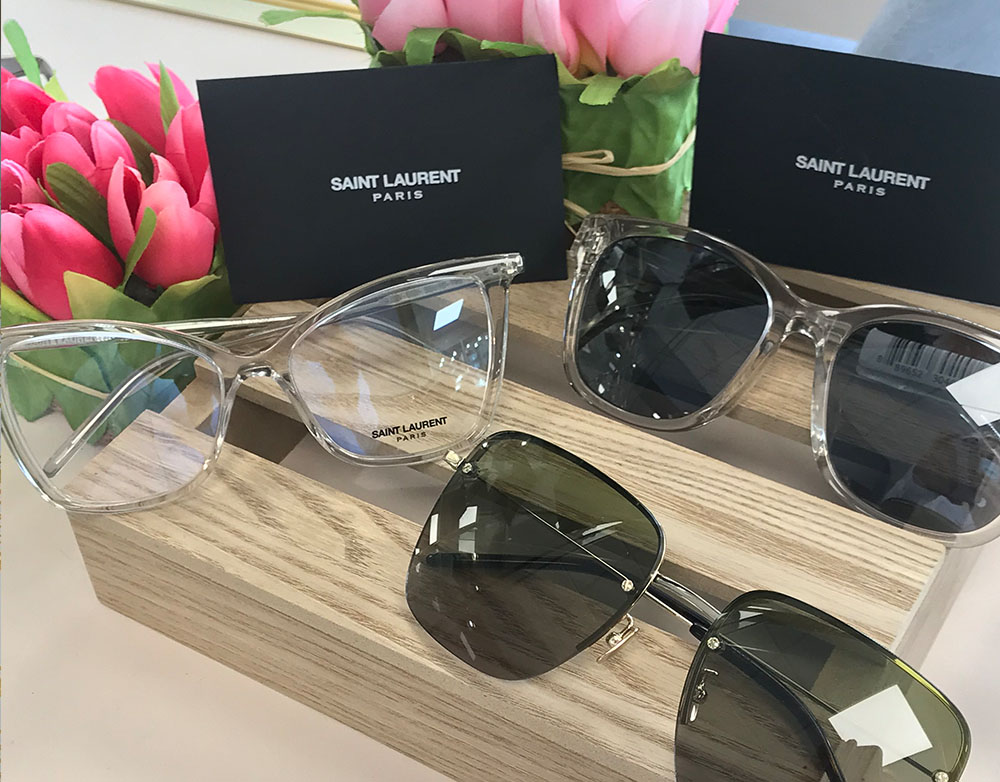 A collection of sunglasses with a Saint Laurent branding tag, displayed on a wooden surface.