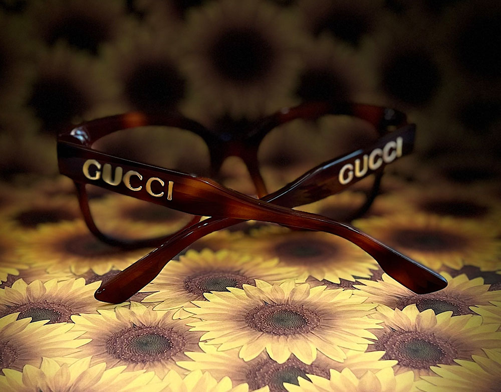 The image features a pair of sunglasses with the word 'GUCCI' printed on the arms, placed over a patterned background.