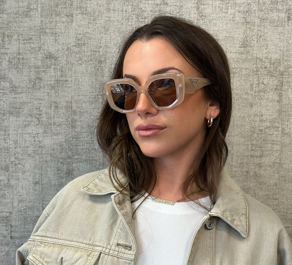 Woman wearing sunglasses, standing against a textured wall.