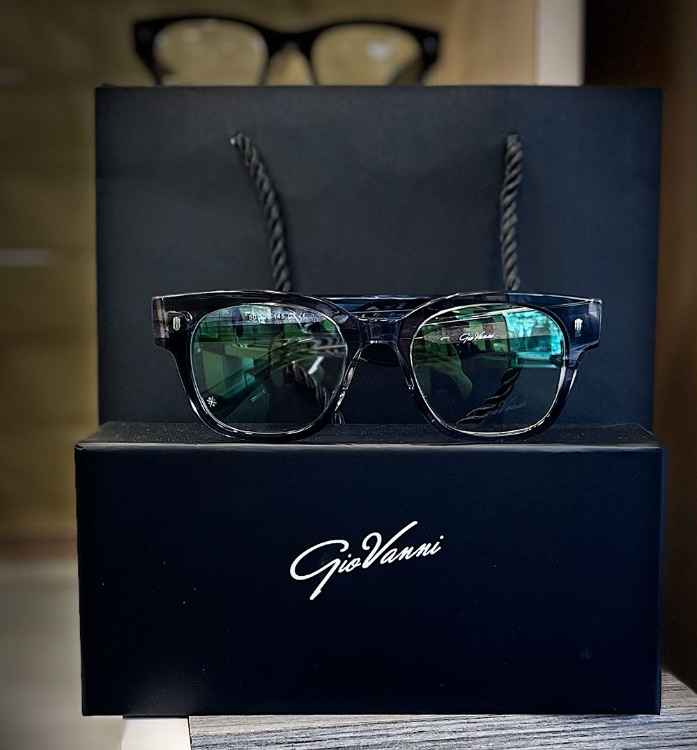A pair of sunglasses with a black frame and green lenses, presented in a black box with the brand name 'GIVANNI' visible on the front.