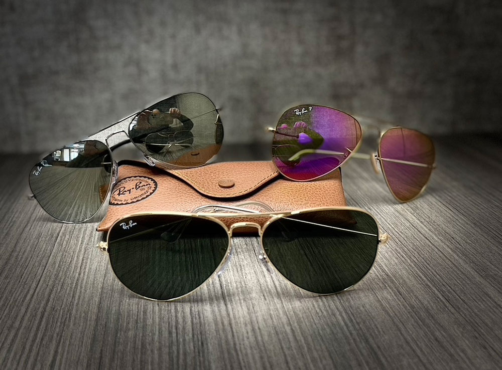 The image displays a collection of sunglasses with various designs and colors, arranged on a surface that appears to be a wooden box or tray.