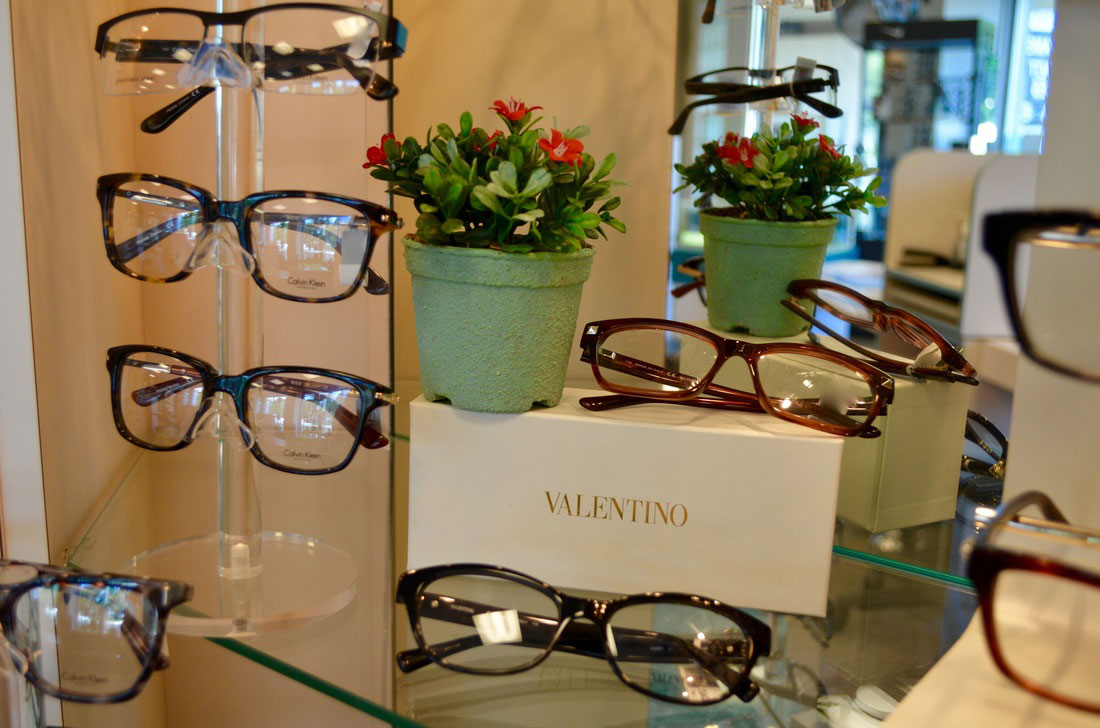 Eyeglasses on display in a store, with a potted plant and a sign with the name Valentino .