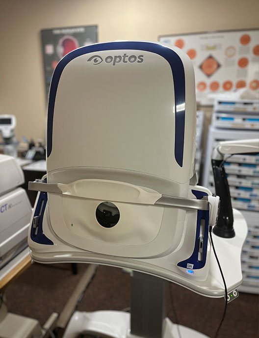 The image depicts an optical machine with a camera attachment, placed on top of a desk in a room that appears to be a medical or dental office.