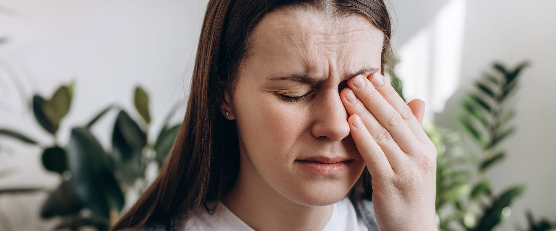 The image shows a person with their hand on their head, looking down and to the side, while holding what appears to be a tissue or napkin.