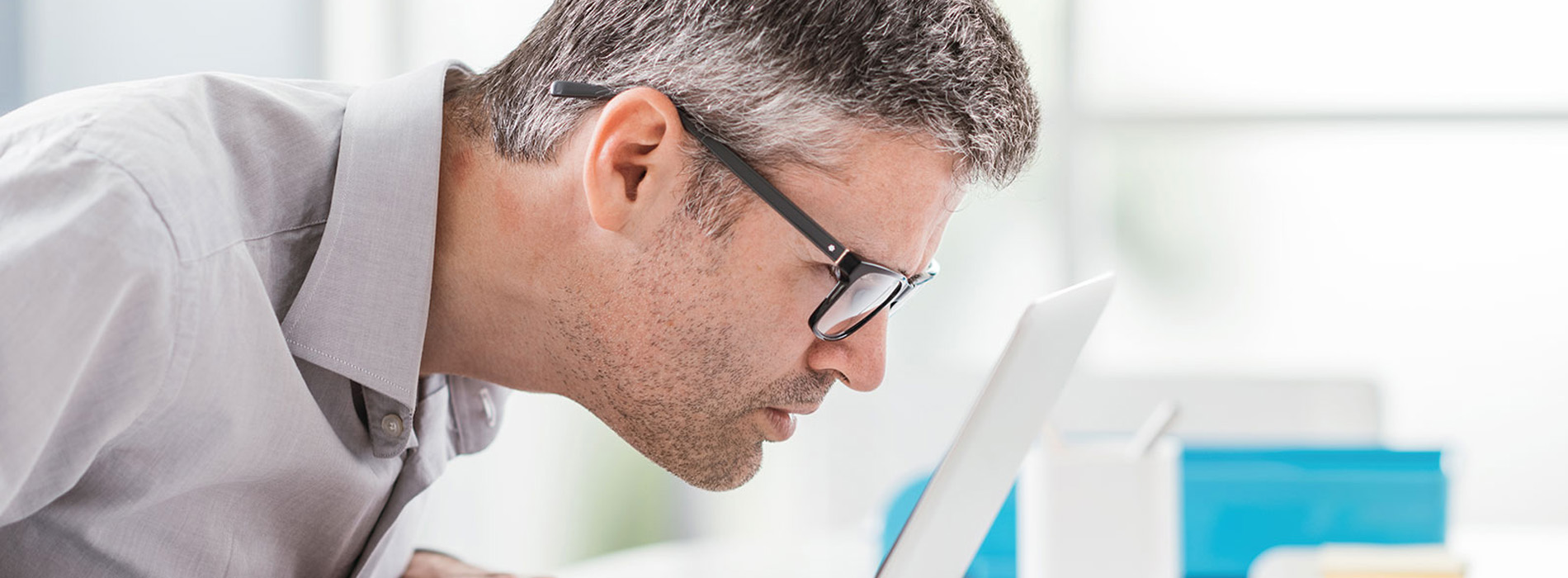 A man in glasses is leaning over a desk, examining a document or object with a focused expression.